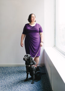 Michelle is standing by a window with her guide dog.