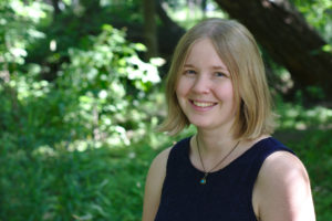 Naomi is smiling and is outside under the trees.