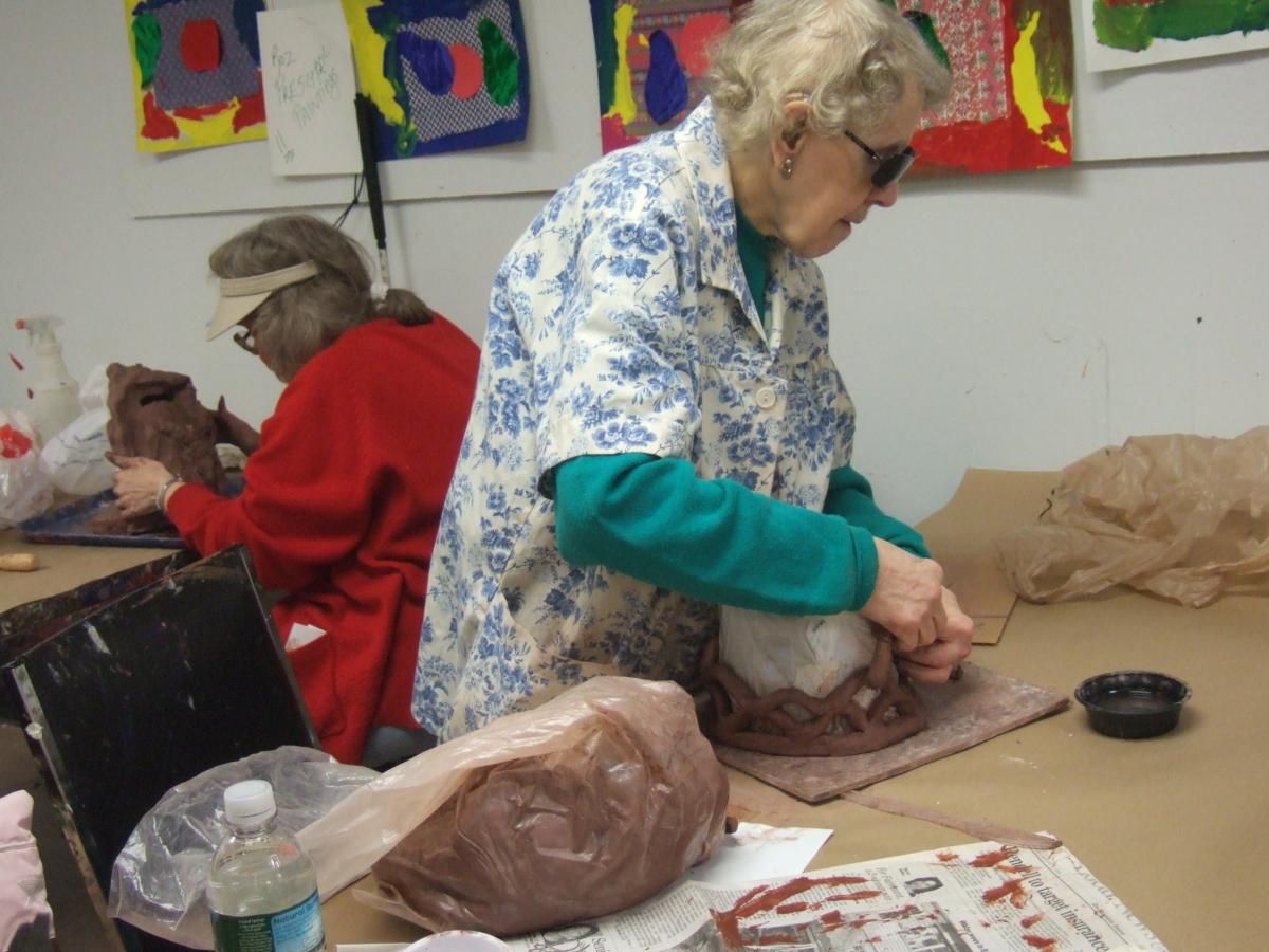 Senior citizen (woman) is working with block of clay in a group setting.