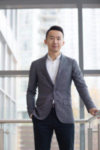 Mark Song is standing by a window in a suit jacket and open-collar shirt.