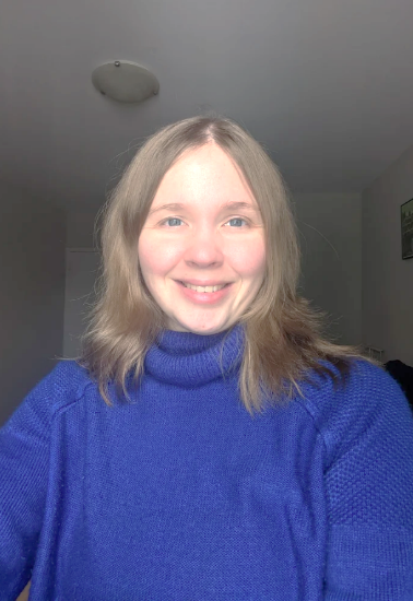 Selfie of Naomi. She is smiling and has shoulder length blonde hair, blue eyes and is wearing a blue sweater.