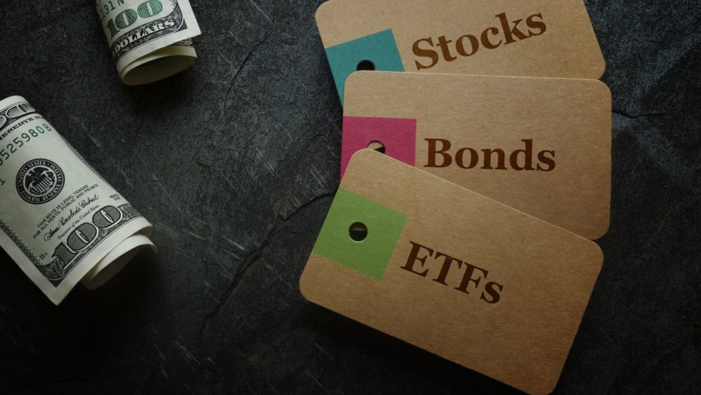Two USD100 bill. 3 brown cards with texts that read, "Stocks, Bonds, ETFs"