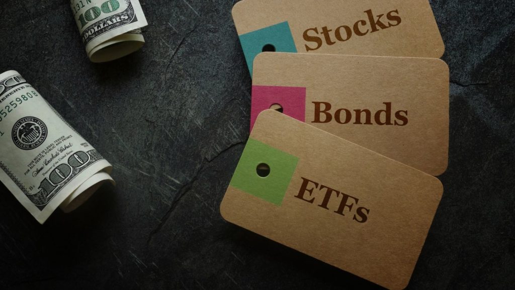 Two USD100 bill. 3 brown cards with texts that read, "Stocks, Bonds, ETFs"