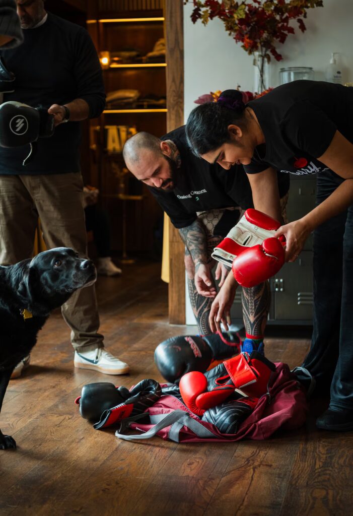 Coach Pharrell Shaymar helps Kamini Rodhan choose boxing gloves as a guide dog stands nearby.